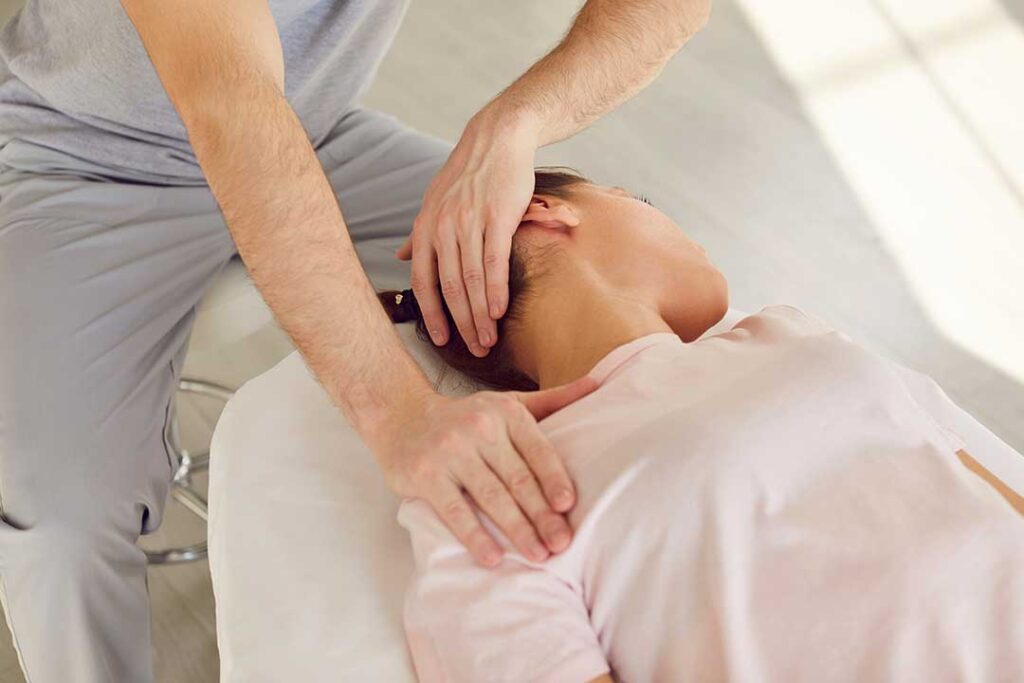 Athlete discussing back stiffness with a chiropractor beside a treatment table in a bright clinic room.